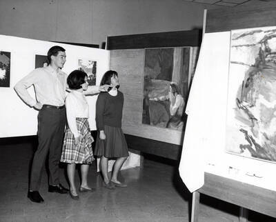 1963 photograph of Art and Architecture. Students Glenn Martz, Carol Doyle and Barbara Feil examining art during an exhibit. Donor: Publications Dept.
