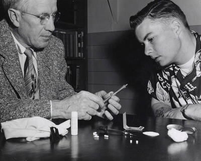 1954 photograph of Sociology Buckled. Prof. Harry C. Harmsworth and Edwin Henry Pfuhl Jr. examine drug paraphernalia