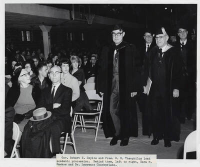 1964 photograph of 75th Anniversary. Governor Robert E. Smylie and President D.R. Theophilus lead a procession in academic regalia. Ezra M. Hawks and Dr. Lawrence H. Chamberlain.