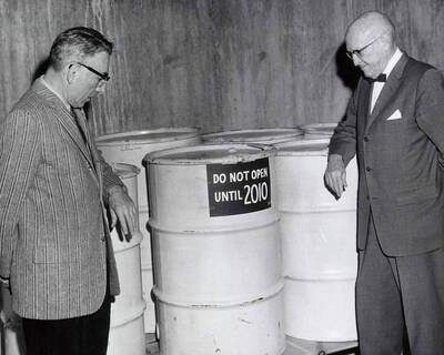 1962 photograph of Gifts. Lee Zimmerman and Donald Theophilus with W. C. Chaney's time capsule barrels. A sign labels them 'Do not open until 2010.'