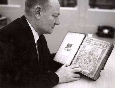 1968 photograph of Gifts. George Kellogg examines a Bible from 1518. Donor: Publications Dept.