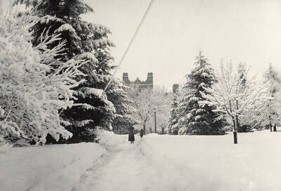 1930 photograph of Administration Building. View of winter scene, student on walkway.