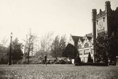 1920 photograph of Administration Building. View of automobiles out front and a student walking to class.