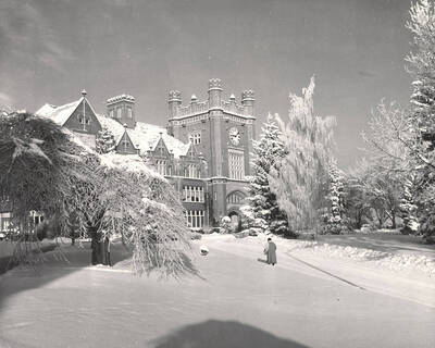 1930 photograph of Administration Building. View of winter scene with student on walkway.