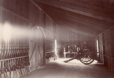 1896 photograph of Armory. View of the rifle lined walls and three cadets. Donor: Gilbert Hogue.