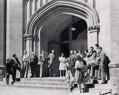 1960 photograph of University of Idaho campus scene. View of students and faculty or administrators next to administration building entrance.