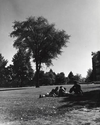 1960 photograph of University of Idaho campus scenery. Students shown sitting on the lawn. Donor: Photo Center.