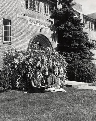 1950 photograph of Forney Hall. Students shown sitting on the lawn. Donor: Publications Dept.
