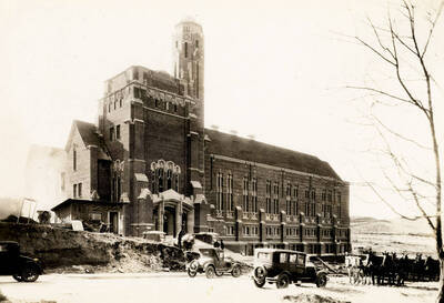 1928 photograph of Memorial Gymnasium. View of automobiles and horse drawn wagons in front.