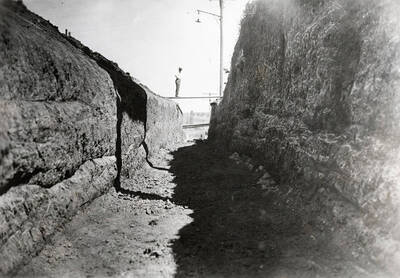 1927 photograph of Excavation for main steam tunnel. View of a man on a board spanning the tunnel.