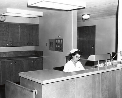 1960 photograph of Infirmary. Nurse sits at nurse's station. Donor: Publications Dept.