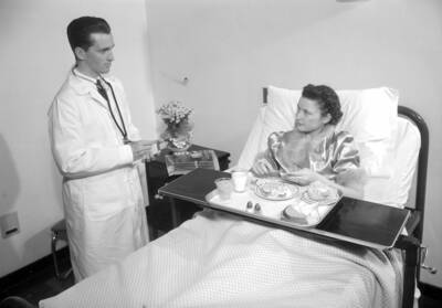 1940 photograph of Infirmary. Doctor specks with a patient.