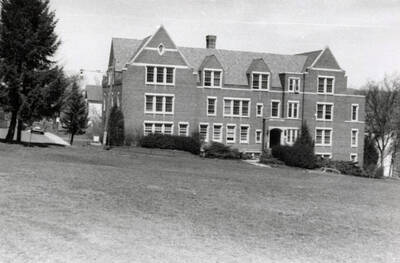 1954 photograph of Infirmary. View from across the lawn, automobiles on the streets.