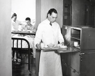 1937 photograph of Infirmary. Food worker distributes meals to the patients.