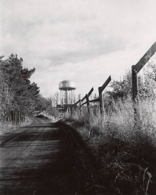 1953 photograph of I Tank. View of a fence lined road.