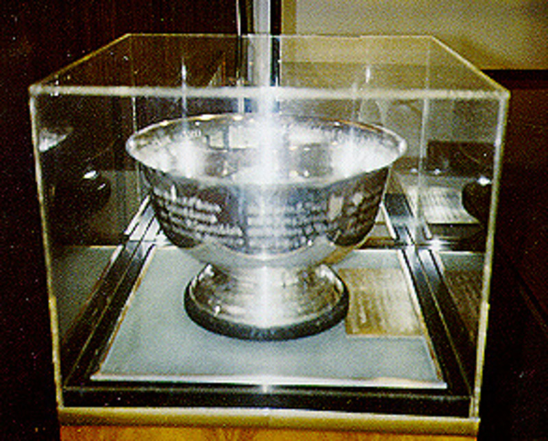 Inscribed silver bowl displayed with an inscription plaque and encased under a plexiglass cover.