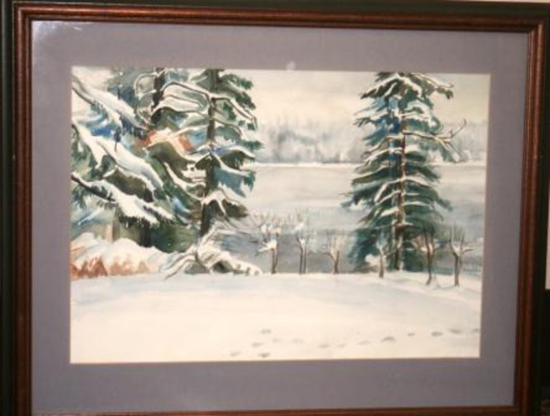 Painting depicting a snowy landscape with a few snow covered trees displayed in a dark brown wood frame with a green trim. The painting is also matted in light blue.
