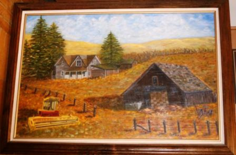 Painting of Martin Farm East of Cottonwood. It depicts two buildings and the farm on a yellow field. This piece is framed in a wood frame.