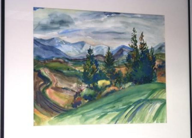 Landscape watercolor painting depicting some trees, a road, green hills, and mountains in the background. This piece is matted in white and displayed in a black metal frame.