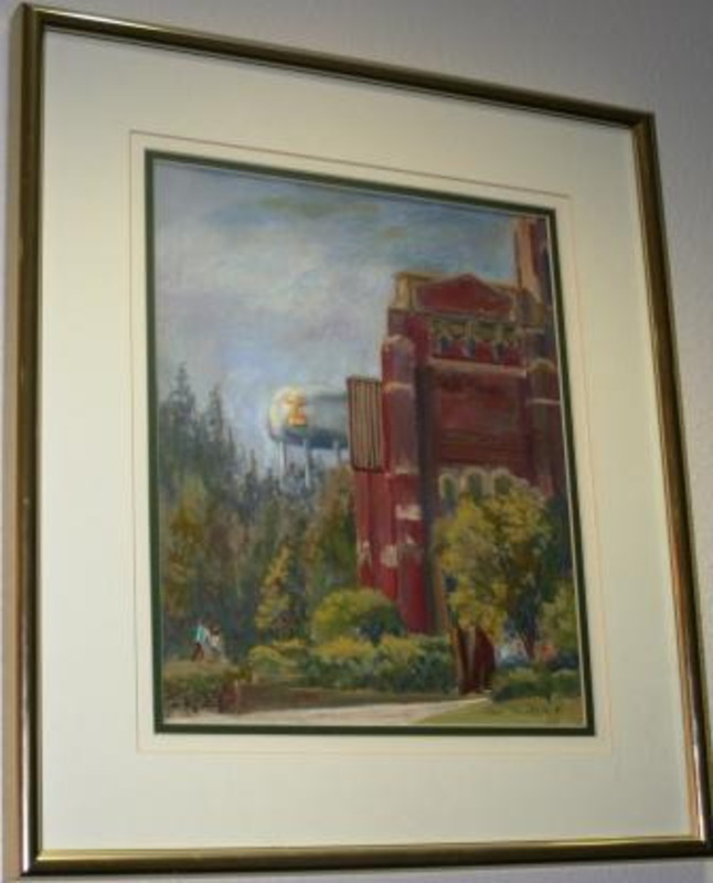 Pastel drawing of the front view of Memorial Gym with the water tower in the background. A few people are walking in the front. It is displayed in a gold frame.