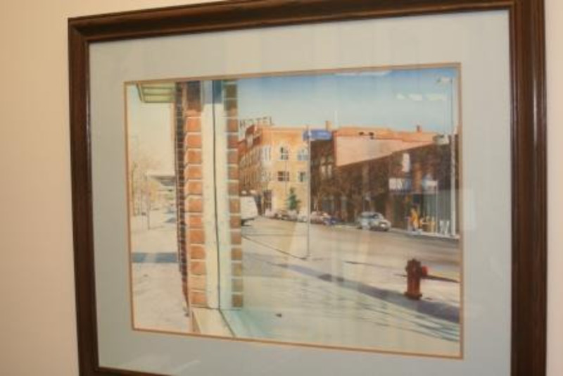 Painting showing the main street of Moscow, Idaho, reflected in a storefront window. Displayed using a cream matte in a thin wooden frame.