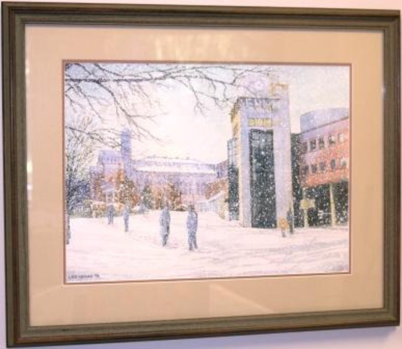 Painting showing students walking outside the University of Idaho Library in a snow covered landscape with the Memorial Gymnasium in the background. Displayed using a cream matte in a grey wooden frame.