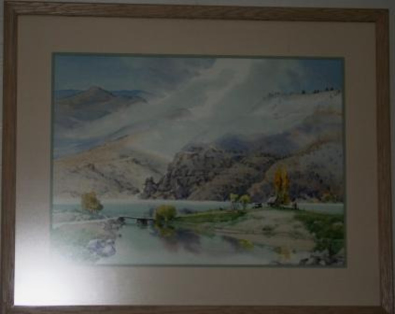 Painting showing a landscape of steep hills above a river spanned by a bridge. Displayed with a tan matte in a cream frame.