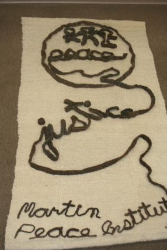 Hand woven wool image showing a circle containing people holding hands and a line forming the words "Peace" and "Justice" with a label reading "Martin Peace Institute."