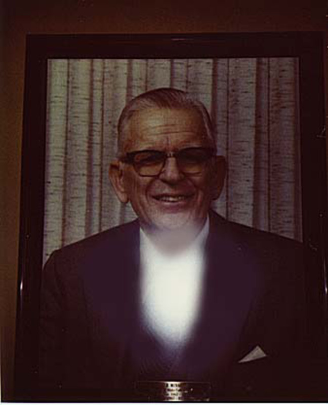 Portrait color photograph of Albert Menard. Displayed under glass in a wooden frame with a plaque.