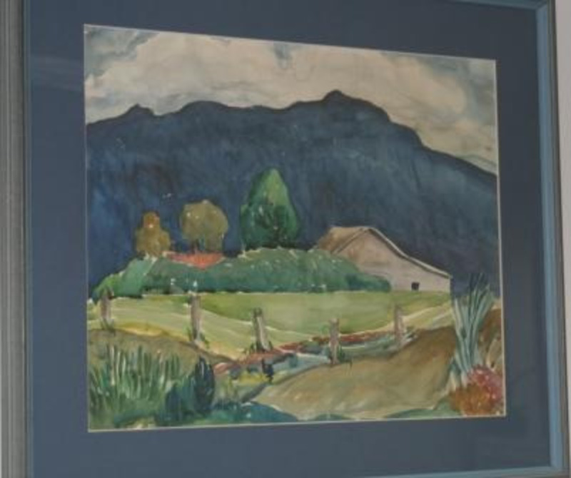 Painting showing a farmstead surrounded by trees and green fields with a dark mountain in the background. Displayed using a dark blue matte in a blue/gray wooden frame.