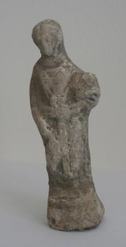Terracotta sculpture of a human figure wearing robes and carrying an object in one arm.