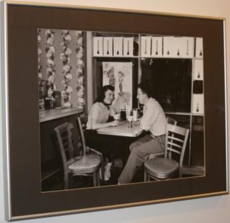 Black and white photograph showing a man and a woman sitting at a table holding drinks.
