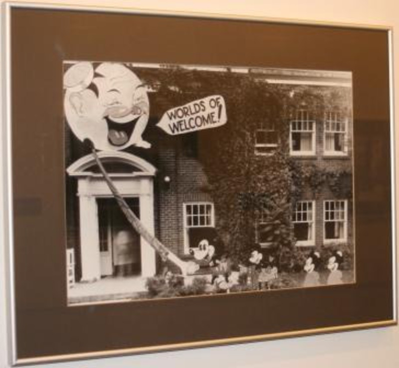 Black and white photograph showing an ivy faced building decorated with a Mickey Mouse theme and a cartoon face saying "Worlds of Welcome!"