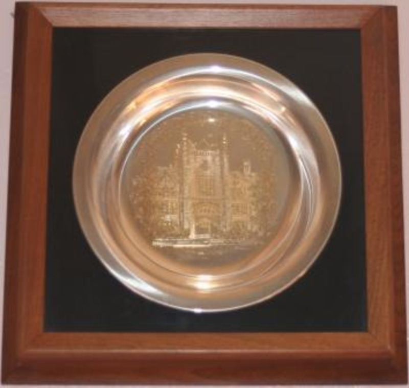 Silver plate inscribed with the image of the University of Idaho Administration Building. Encased in plexiglass with a black background and wooden frame.