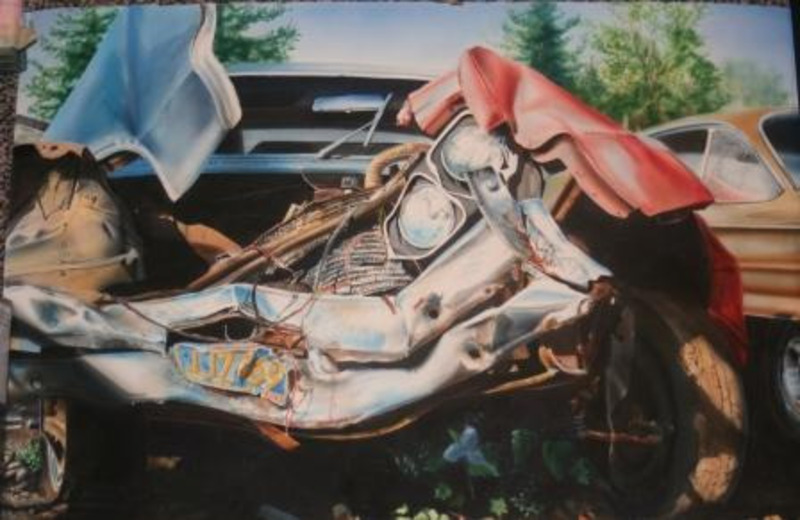 Painting depicts old damaged cars in a junkyard small flowers in the foreground and trees in the background.