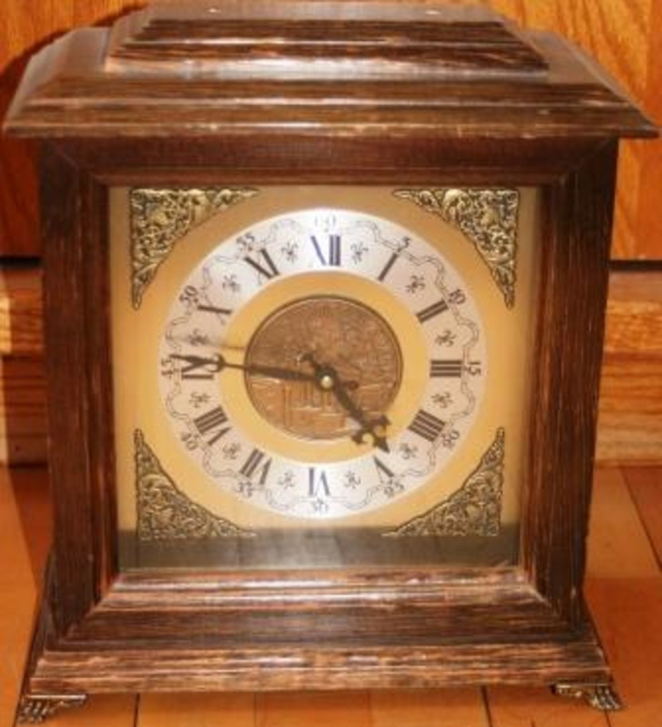 Wood bodied mechanical clock with an ornate metal face. An inscription on the face reads "University of Delaware."