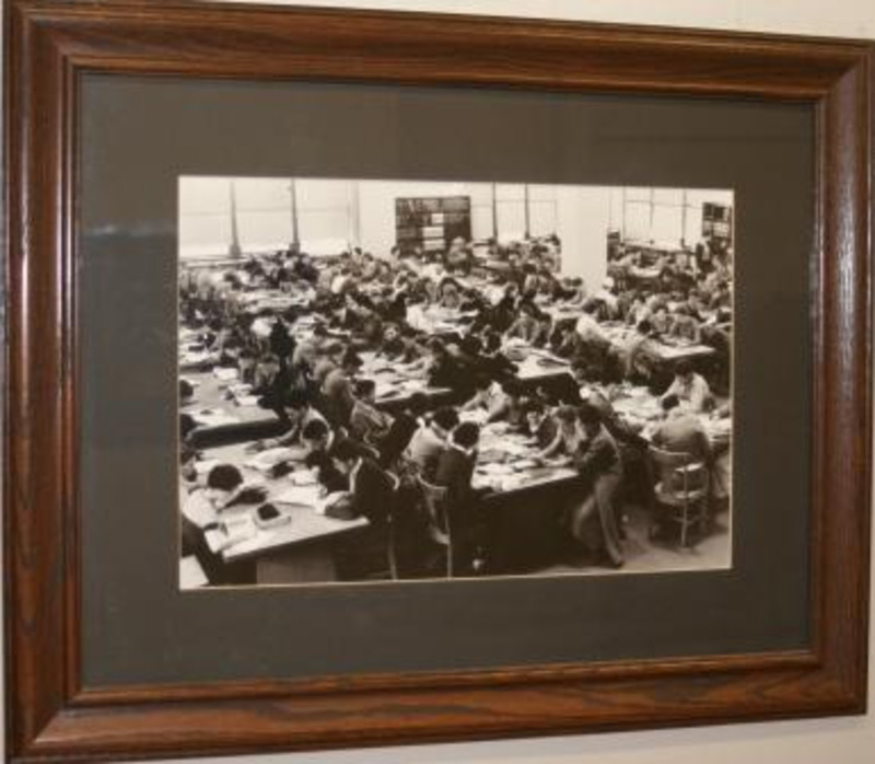 Black and white photograph of students working at tables in the library reading room in 1934. The photograph is displayed with a black matte in a wooden frame.