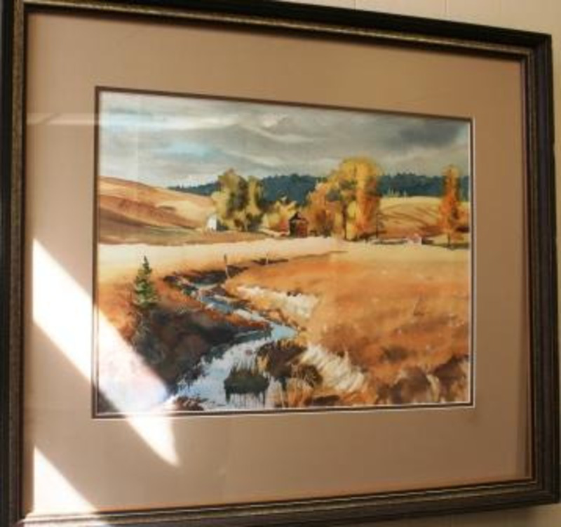 Painting of a country landscape showing a flowing creek, golden fields, weathered buildings, autumnal trees, and dark distant mountains. The painting is displayed using a tan matter, dark brown trim matte, and a gilt wooden frame.
