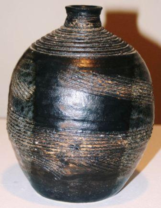 Stoneware vase with parallel grooves and a dark finish. "UI Grad Student" is written on the bottom of the vase.