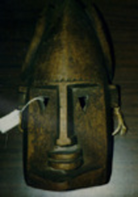 Carved wooden mask of a head with three points and triangular eyes.