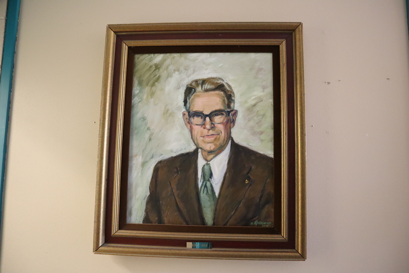 Painted portrait of Dr. Glenn Holm wearing a brown suit and green tie.