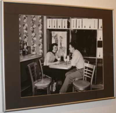 Black and white photograph showing a man and a woman sitting at a table holding drinks.