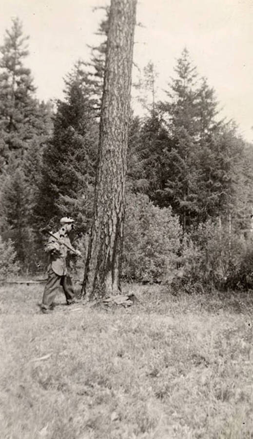 A CCC man posing with an axe in front of a tall pine tree. Writing below the photo reads: 'McMann'.