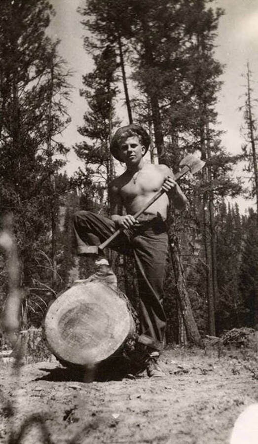 A CCC man posing with an axe over a log. Writing below the photo reads: 'Him Again'.