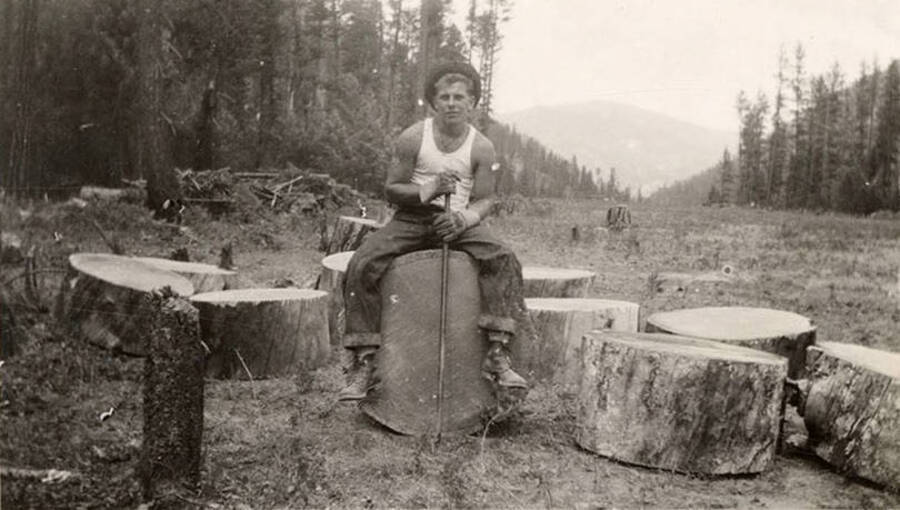 A CCC man sitting on a logged tree holding an axe, other circular pieces of the log sit around him. Writing below the photo reads: 'Bobbs'. Writing under a duplicate photo reads: ''Bubby' Kesaday'.