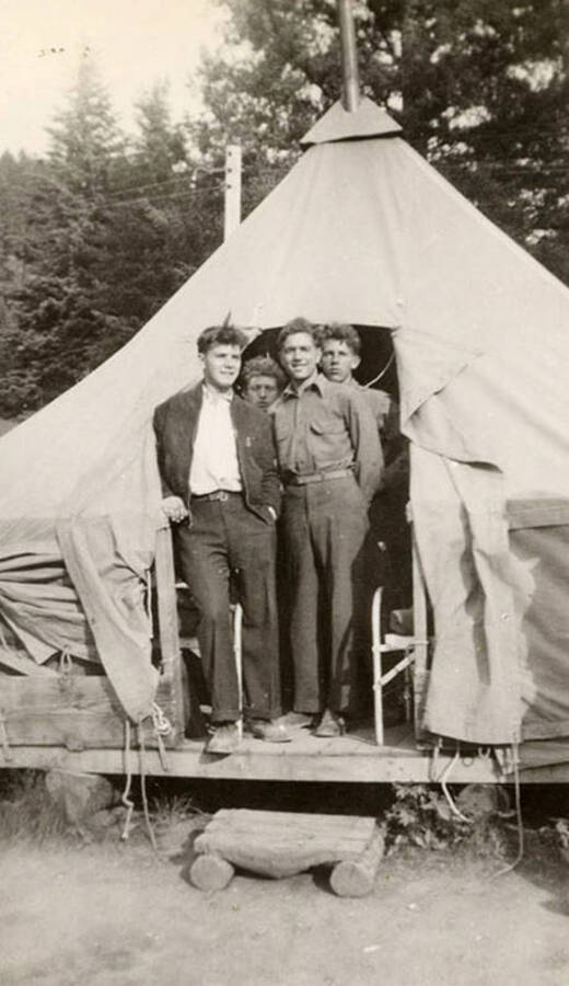 A group of four CCC men crowded into the entrance of a tent barrack.