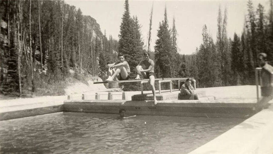 Several CCC men relaxing at Warm Lake Swimming Pool on the diving board. Writing underneath each photo is a phrase that makes the sentence: 'A couple of the boys relaxing warm lake pool.' Phrase on this image is: 'the boys'.