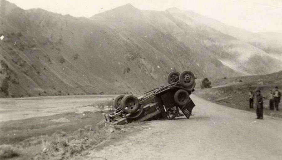 Photo of a truck overturned near the river. Writing underneath each photo is a word that makes the phrase: 'In Riggins.' Word on this image is: 'Riggins'.