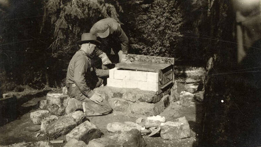 Two CCC men constructing an outdoor stove. Writing under the photo reads: 'John and Frank'.