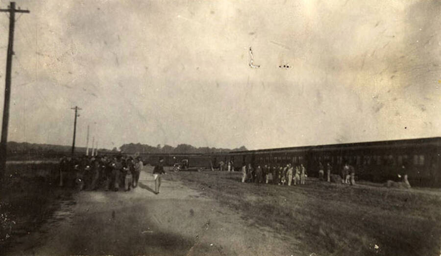 Traveling CCC men in formation at Fort Dix with the train in the background. Writing under the photo reads: ''All off' at Fort Dix'.